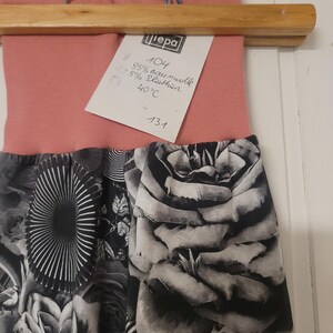 Puede incluir: Un pantal&oacute;n con una cintura de color rosa empolvado y una secci&oacute;n inferior con estampado en blanco y negro con dise&ntilde;os florales y abstractos. Tiene una etiqueta blanca con el texto "Liepa 104 95% Baumwolle 5% Elasthan 40&deg;C 131".