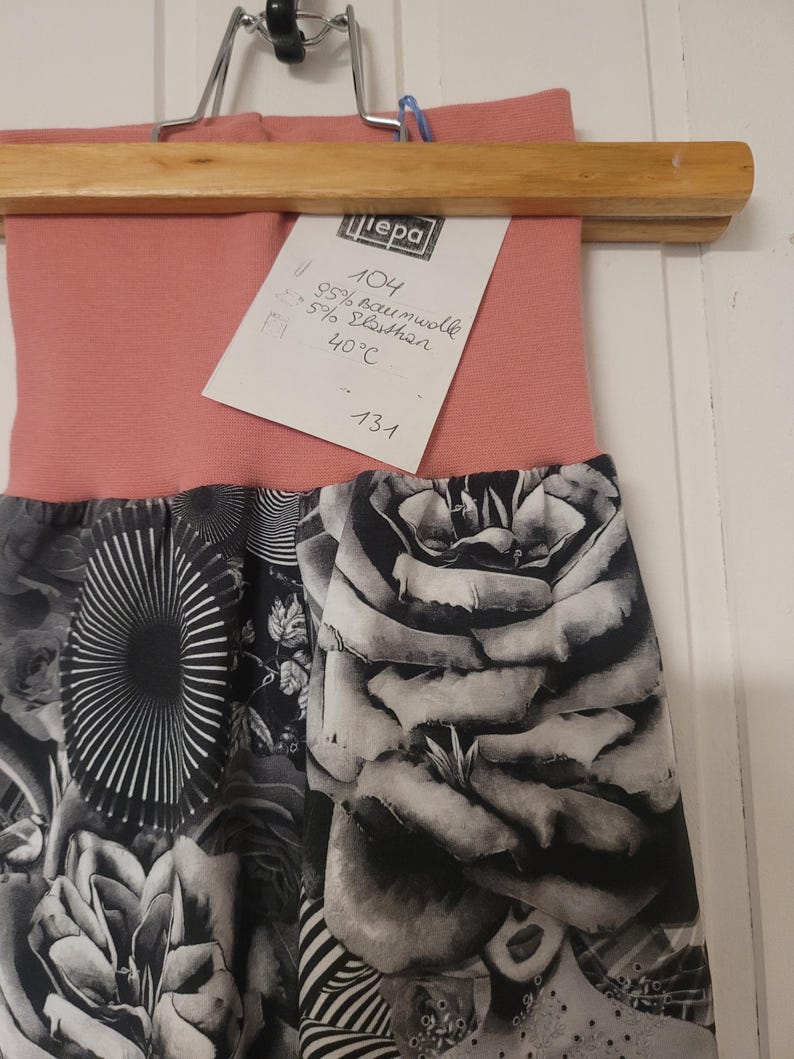 Puede incluir: Un pantal&oacute;n con una cintura de color rosa empolvado y una secci&oacute;n inferior con estampado en blanco y negro con dise&ntilde;os florales y abstractos. Tiene una etiqueta blanca con el texto "Liepa 104 95% Baumwolle 5% Elasthan 40&deg;C 131".