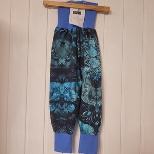 Puede incluir: Pantalones azules con un patr&oacute;n floral y geom&eacute;trico oscuro e intrincado en tonos verde azulado y negro. La prenda tiene una cintura el&aacute;stica ancha de color azul s&oacute;lido y pu&ntilde;os acanalados azules a juego en los tobillos. Una etiqueta blanca con texto est&aacute; sujeta a la cintura.