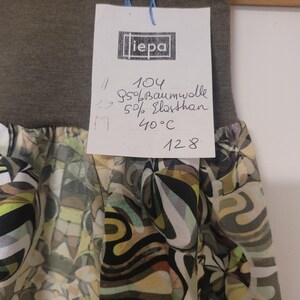 Puede incluir: Una falda con una cintura el&aacute;stica ancha de color verde oliva oscuro y una secci&oacute;n inferior estampada con formas abstractas en tonos verde oliva, negro, blanco y amarillo p&aacute;lido. Una etiqueta blanca muestra el texto iepa, 104, 95% Baumwolle, 5% Elasthan, 40&deg;C y 128.