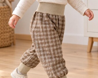 Puede incluir: Pantalones con estampado de cuadros vichy en marrón y beige, con una cintura alta y ancha de canalé en color sólido y puños de canalé a juego en los tobillos. Los pantalones tienen una silueta holgada y se combinan con una camiseta color crema.