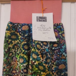 Puede incluir: Un pantal&oacute;n con una cintura ancha de color rosa empolvado y un estampado floral multicolor con tonos verdes, azules y amarillos. Una etiqueta blanca sujeta con un cordel naranja muestra el texto iepa, 104, 95% Baumwolle, 5% Elasthan, 40&deg;C y 132.