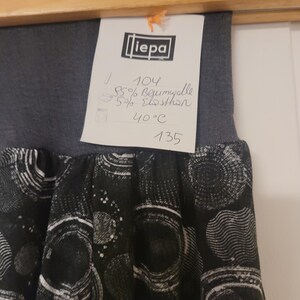 Puede incluir: Una falda gris oscuro con una cintura el&aacute;stica ancha y un panel de tela negra con un patr&oacute;n circular blanco. Se adjunta una etiqueta blanca que muestra la marca "liepa", talla 104, 95% algod&oacute;n, 5% elastano y una instrucci&oacute;n de lavado de 40&deg;C.
