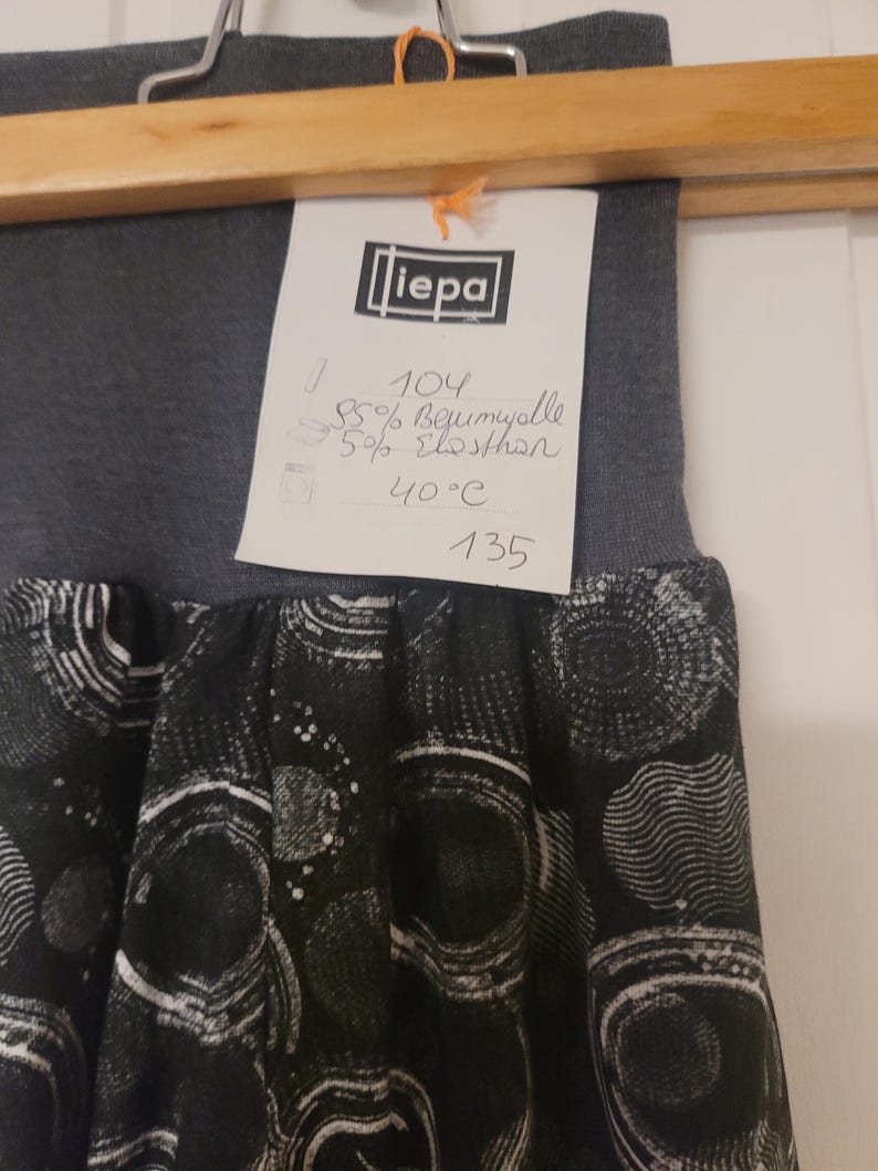 Puede incluir: Una falda gris oscuro con una cintura el&aacute;stica ancha y un panel de tela negra con un patr&oacute;n circular blanco. Se adjunta una etiqueta blanca que muestra la marca "liepa", talla 104, 95% algod&oacute;n, 5% elastano y una instrucci&oacute;n de lavado de 40&deg;C.
