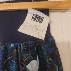 Puede incluir: Una falda azul oscuro con cintura alta y un estampado bot&aacute;nico de aves blancas y helechos azules. Tiene una etiqueta blanca con el nombre "liepa", la composici&oacute;n de 95% algod&oacute;n y 5% elastano, y una instrucci&oacute;n de lavado a 40&deg;C.