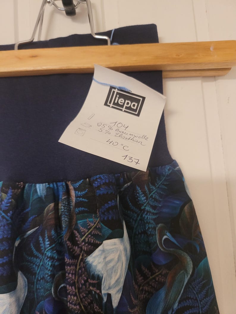Puede incluir: Una falda azul oscuro con cintura alta y un estampado bot&aacute;nico de aves blancas y helechos azules. Tiene una etiqueta blanca con el nombre "liepa", la composici&oacute;n de 95% algod&oacute;n y 5% elastano, y una instrucci&oacute;n de lavado a 40&deg;C.