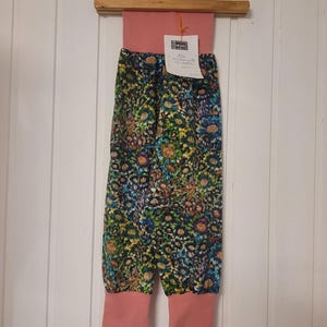 Puede incluir: Pantalones con una cintura ancha de color rosa empolvado liso y pu&ntilde;os a juego en los tobillos. El cuerpo principal presenta un denso estampado floral multicolor en tonos azules, verdes, amarillos y morados. Incluye una etiqueta blanca con texto negro.