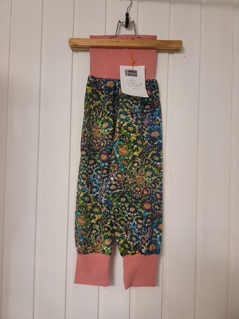 Puede incluir: Pantalones con una cintura ancha de color rosa empolvado liso y pu&ntilde;os a juego en los tobillos. El cuerpo principal presenta un denso estampado floral multicolor en tonos azules, verdes, amarillos y morados. Incluye una etiqueta blanca con texto negro.