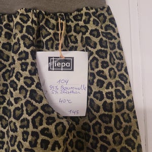 Puede incluir: Una falda con estampado de leopardo en verde oliva y negro con una cintura el&aacute;stica en verde oliva s&oacute;lido. Una etiqueta blanca unida con un cordel muestra el texto "iepa", "104", "95% Baumwolle", "5% Elasthan", "40&deg;C" y "145".