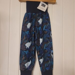 Puede incluir: Pantalones con fondo azul oscuro y un patr&oacute;n repetitivo de grullas blancas y hojas de helecho azules. La prenda tiene una cintura el&aacute;stica ancha de color azul oscuro s&oacute;lido y pu&ntilde;os acanalados a juego en los tobillos. Se incluye una etiqueta blanca con el texto "iepa".