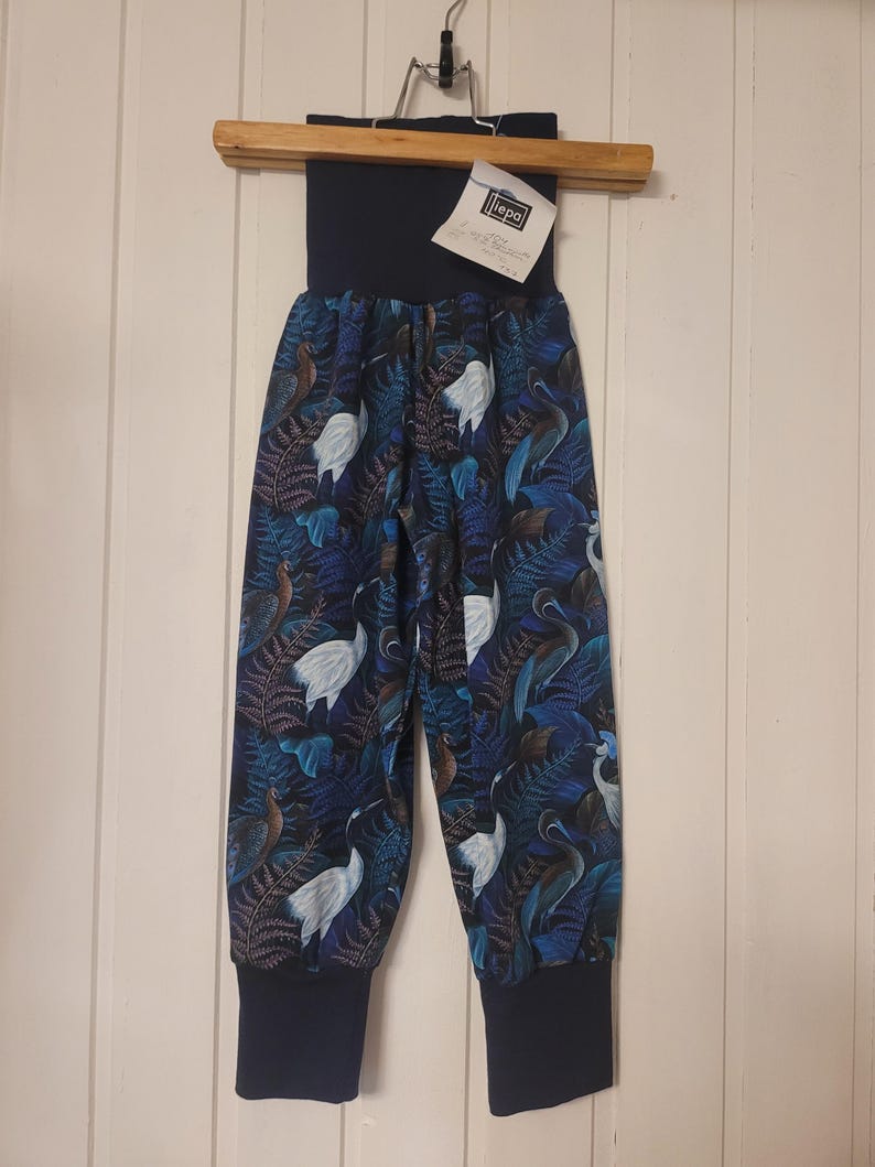 Puede incluir: Pantalones con fondo azul oscuro y un patr&oacute;n repetitivo de grullas blancas y hojas de helecho azules. La prenda tiene una cintura el&aacute;stica ancha de color azul oscuro s&oacute;lido y pu&ntilde;os acanalados a juego en los tobillos. Se incluye una etiqueta blanca con el texto "iepa".