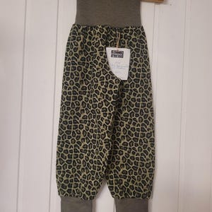 Puede incluir: Pantalones con estampado de leopardo en tonos negro, marr&oacute;n y verde oliva. La prenda incluye una cintura el&aacute;stica ancha de color verde oliva s&oacute;lido y pu&ntilde;os a juego en los tobillos. Una etiqueta blanca est&aacute; sujeta en la parte delantera.