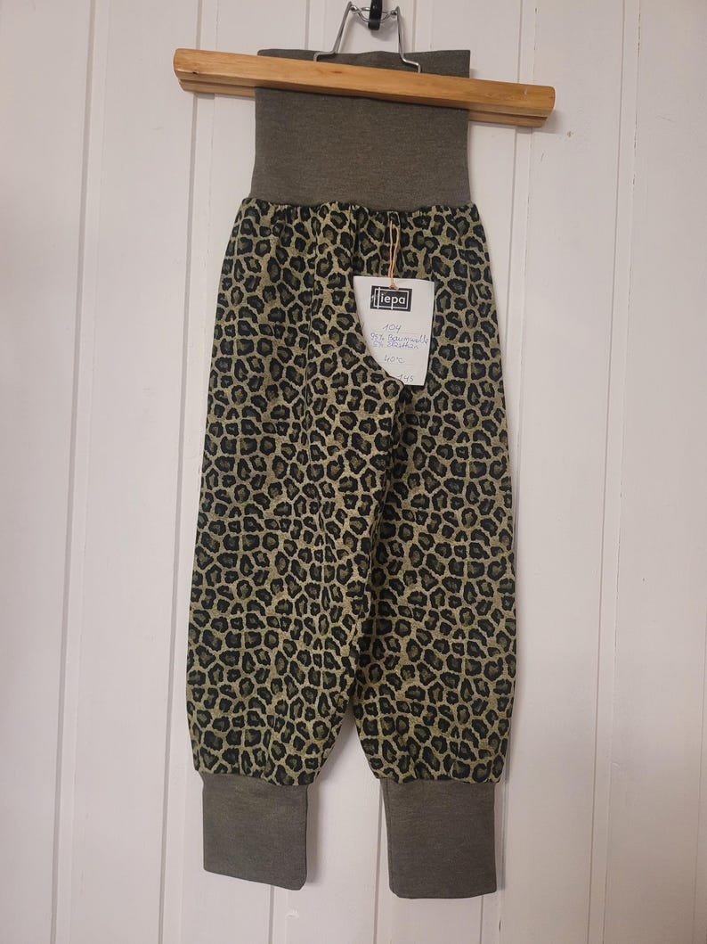 Puede incluir: Pantalones con estampado de leopardo en tonos negro, marr&oacute;n y verde oliva. La prenda incluye una cintura el&aacute;stica ancha de color verde oliva s&oacute;lido y pu&ntilde;os a juego en los tobillos. Una etiqueta blanca est&aacute; sujeta en la parte delantera.