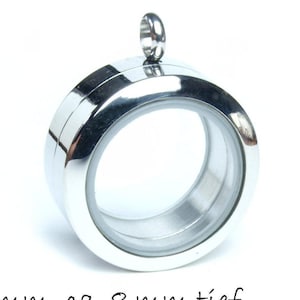 Op de afbeelding: Een zilverkleurige, ronde medaillonhanger met een helder glazen midden. De hanger heeft een diameter van ongeveer 1,9 cm en is 0,8 cm diep. Hij heeft een kleine lus aan de bovenkant voor een ketting.