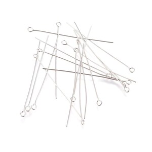 May include: A pile of silver-toned head pins with small loops at the top. The pins are scattered on a white background.