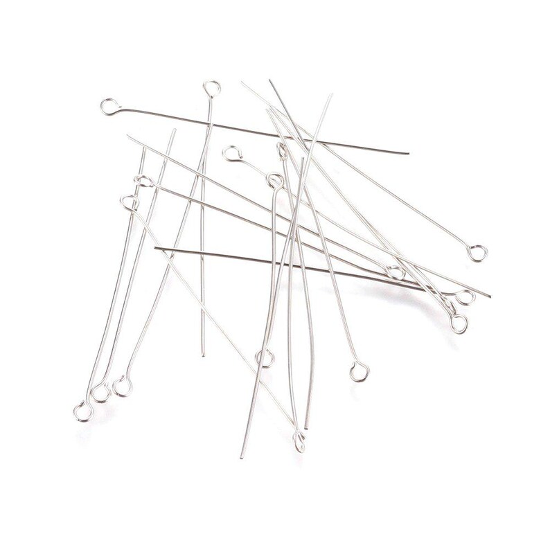 May include: A pile of silver-toned head pins with small loops at the top. The pins are scattered on a white background.