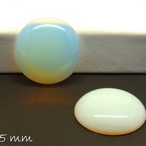 Könnte beinhalten: Zwei ovale Opal-Cabochons, einer mit einem hellblauen und gelben irisierenden Schimmer und der andere mit einem weißen irisierenden Schimmer. Die Cabochons haben einen Durchmesser von 25 mm.