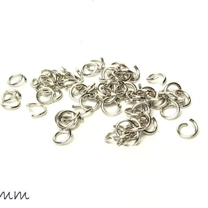 Op de afbeelding: Een stapel zilveren springringen, elk met een diameter van 4 mm. De ringen zijn verspreid over een witte achtergrond.