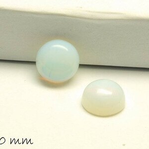 Könnte beinhalten: Zwei weiße Opal-Cabochons, einer ist etwas größer als der andere. Der größere Cabochon hat einen Durchmesser von 10 mm.