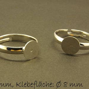 Könnte beinhalten: Zwei verstellbare Ringrohlinge aus Silber mit einer runden, flachen Klebefläche. Die Ringrohlinge haben einen Durchmesser von 17 mm und die Klebefläche einen Durchmesser von 8 mm.