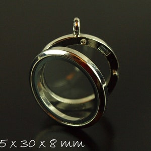 Könnte beinhalten: Silberner Anhänger mit einem transparenten Glaseinsatz. Das Medaillon ist geöffnet und das Innere ist sichtbar. Das Medaillon misst 35,5 x 30 x 8 mm.