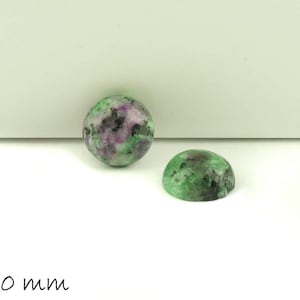 Könnte beinhalten: Zwei grüne, rosa und schwarze Cabochon-Edelsteine, jeder mit einem Durchmesser von 10 mm. Die Edelsteine sind rund und haben eine glatte, polierte Oberfläche.