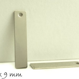 Può includere: Due etichette rettangolari in metallo argentato con un foro nella parte superiore. L'etichetta più grande misura 40 mm per 9 mm.