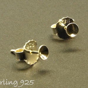 Könnte beinhalten: Zwei silberne Ohrstecker mit einem runden, flachen Kopf. Die Rückseite jedes Steckers ist mit "925" geprägt, was Sterlingsilber anzeigt.