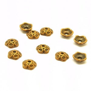 Könnte beinhalten: Eine Gruppe von 10 goldfarbenen Metallperlenkappen mit einem dekorativen Design. Die Kappen haben ein rundes Loch in der Mitte und ein blumenartiges Design um das Loch herum.
