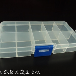 Könnte beinhalten: Eine transparente Kunststoff-Aufbewahrungsbox mit 9 Fächern und einem blauen Verschluss. Die Box misst 13 x 6,8 x 2,1 cm.