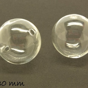 Könnte beinhalten: Zwei klare Glassphären mit einem Durchmesser von 30 mm. Die Sphären sind glatt und haben einen leichten Glanz.