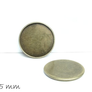 Könnte beinhalten: Zwei runde, metallische, leere, 25 mm große Rohlinge zum Schmuckmachen.