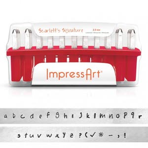 Può includere: Un set di timbri per lettere in metallo da 2,5 mm in una custodia di plastica trasparente con base rossa. La custodia ha il testo "Scarlett's Signature" e "Impress Art" stampato su di essa. I timbri includono l'alfabeto, i numeri, i segni di punteggiatura e i simboli.