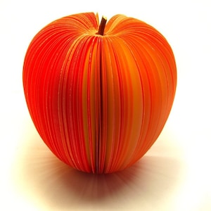 Könnte beinhalten: Ein orangefarbener Papierapfel aus gefalteten Papierstreifen. Der Apfel ist ein Dekorationsobjekt.
