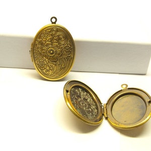 Könnte beinhalten: Ein ovales Medaillon in Goldton mit einem floralen Design. Das Medaillon ist geöffnet und zeigt ein leeres Inneres.