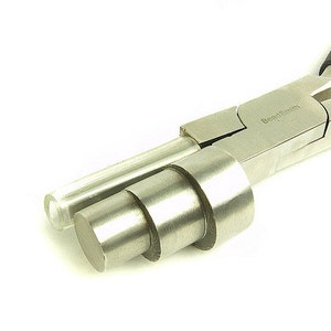 Puede incluir: Primer plano de unas pinzas para hacer cuentas de plata con mango negro. Las pinzas están abiertas y tienen un juego de mandriles en su interior. Los mandriles se utilizan para crear bucles de diferentes tamaños para la elaboración de joyas. Las pinzas están etiquetadas como "BeadSmith".