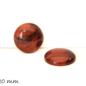 Könnte beinhalten: Zwei runde, rot-braune Cabochons, jeweils 20 mm im Durchmesser. Die Steine haben eine glänzende Oberfläche und ein wirbelndes Muster.