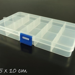 May include: A clear plastic storage box with a blue latch. The box has 10 compartments and measures 17.5 x 10 cm.