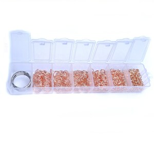 May include: A clear plastic storage box with eight compartments filled with gold jump rings. The box is open and the jump rings are visible.