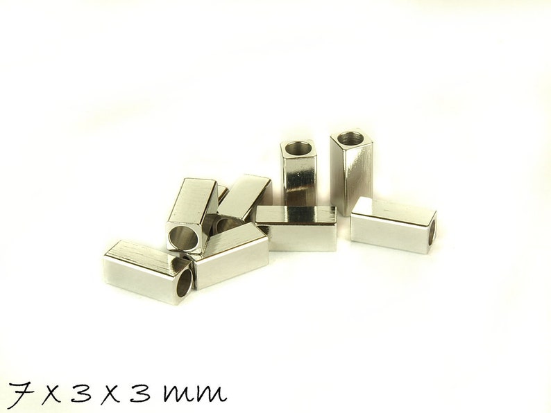 May include: A group of silver metal spacer beads, each measuring 7mm x 3mm x 3mm. The beads are rectangular in shape with a hole in the center.