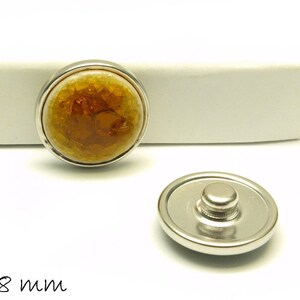 Könnte beinhalten: Eine 18 mm Druckknopf mit einer braunen und goldenen Harz-Einlage. Der Knopf ist aus Metall und hat eine silberne Oberfläche.