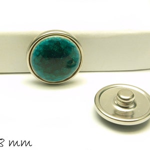 May include: A teal blue snap button with a silver metal backing. The button is 18 mm in diameter.