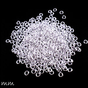 May include: A large pile of silver jump rings, each measuring 3 mm in diameter. The rings are scattered on a black background.