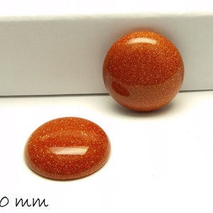 Könnte beinhalten: Zwei orangefarbene, runde, glitzernde Cabochons mit einem Durchmesser von jeweils 20 mm. Die Cabochons liegen auf einer weißen Oberfläche.