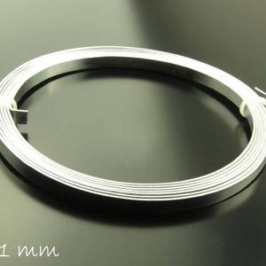 Könnte beinhalten: Eine Spule aus silberfarbenem Metalldraht, 5 Millimeter breit und 1 Millimeter dick. Der Draht ist zu einem Kreis gewickelt und liegt auf einer schwarzen Oberfläche.