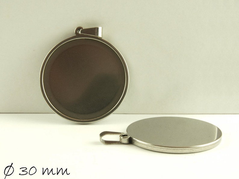 May include: Two silver round metal pendants with a diameter of 30 mm. The pendants have a smooth, shiny surface and a loop at the top for attaching to a chain or cord.