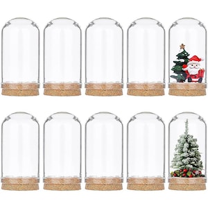 Puede incluir: Una colección de campanas de cristal con bases de corcho. Algunas campanas contienen árboles de Navidad en miniatura y figuras de Papá Noel, mientras que otras están vacías. El cristal transparente permite ver el contenido, ideal para la decoración navideña.