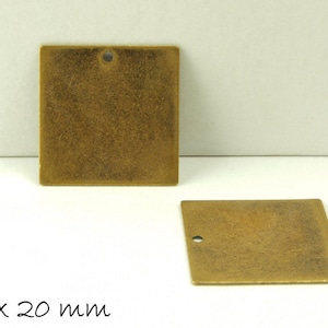 Könnte beinhalten: Zwei quadratische Metallanhänger mit einem Loch in der Mitte. Die Anhänger sind 20 mm x 20 mm groß und haben eine gebürstete Goldoberfläche.