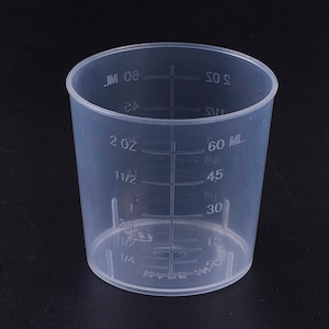 Op de afbeelding: Een doorzichtige kunststof maatbeker met markeringen in ounces en milliliters. De beker heeft een capaciteit van 2 ounces of 60 milliliters.