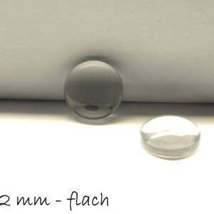 Könnte beinhalten: Zwei transparente Glascabochons, einer mit grauer Rückseite, mit einem Durchmesser von 12 mm. Der Text "Ø 12 mm - flach" ist unter den Cabochons sichtbar.